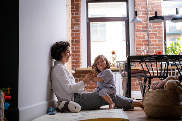 Hijita y mamá jugando en casa sentadas en el suelo madre e hija riéndose divirtiéndose juntas