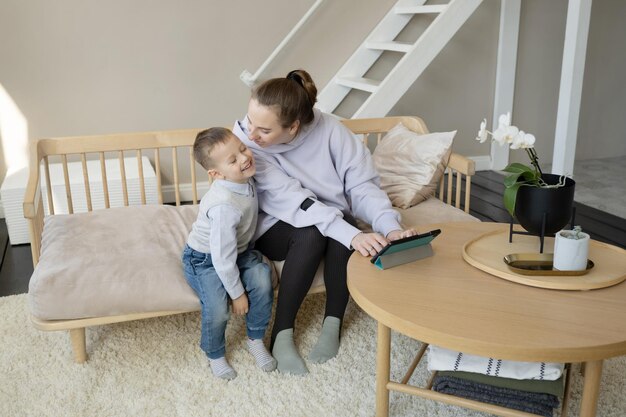 El hijo abraza a su madre y observa a su madre trabajando en una tableta.