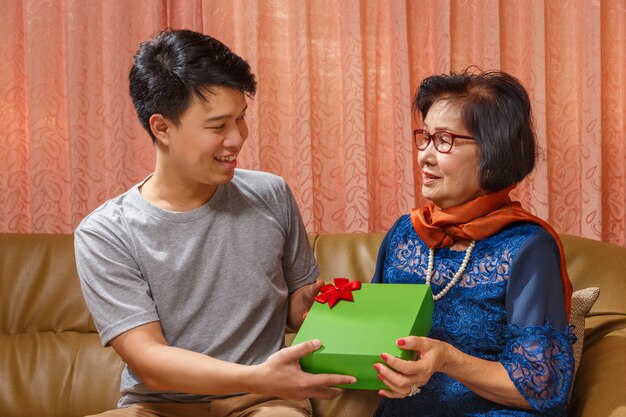 Foto hijo adulto da un regalo a la madre en el día de la madre.