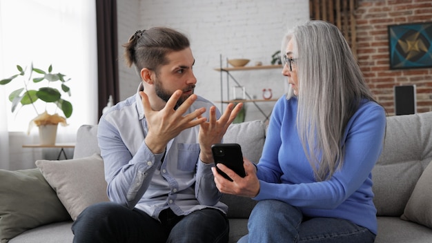 Foto hijo adulto enseñando a su madre mayor a usar aplicaciones móviles de teléfonos inteligentes compartiendo fotos de compras en línea