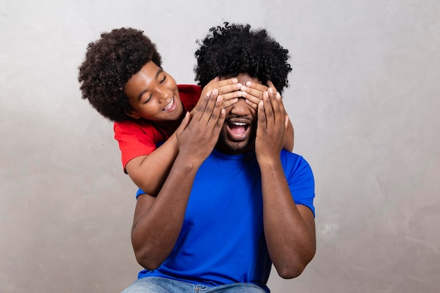 Hijo afro cubriendo los ojos de su padre con la mano para hacer una sorpresa el Día del Padre