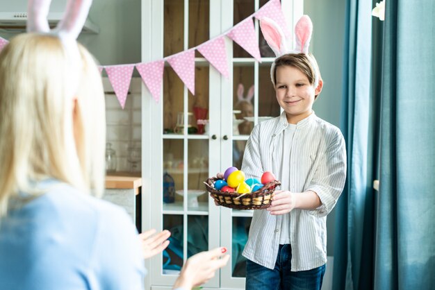 El hijo le da a mamá una canasta de huevos de Pascua. Hijo de cerca.