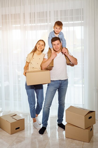 Hijo de familia y niño feliz en el contexto de ventanas panorámicas. Mujer sosteniendo una caja de cartón