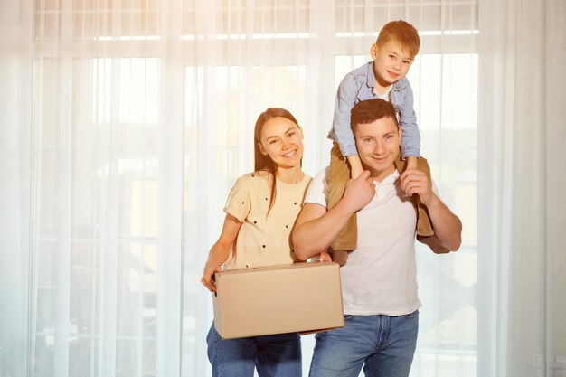 Hijo de familia y niño feliz en el contexto de ventanas panorámicas. Mujer sosteniendo una caja de cartón