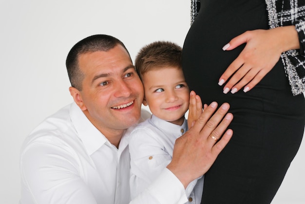 Foto hijo feliz y padre escucha y sostiene sus manos en el estómago de su madre embarazada