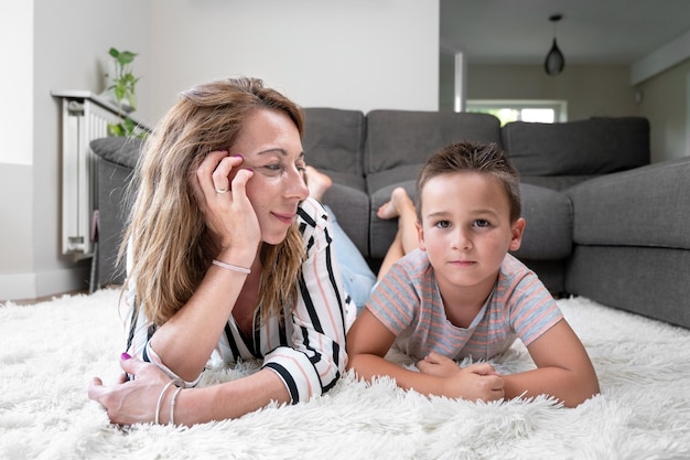 Foto hijo y madre acostados juntos en una alfombra blanca mirándose el uno al otro