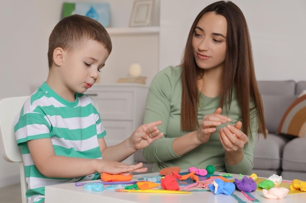 Hijo y madre esculpindo con masa de juego en la mesa en el interior