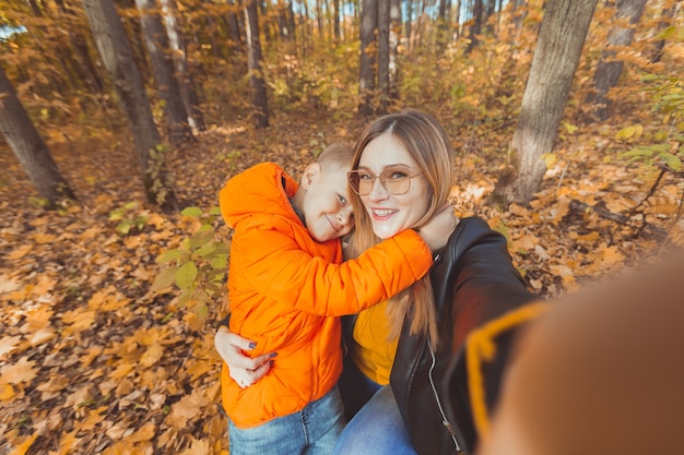 Hijo y madre están tomando selfie en cámara en otoño parque ocio monoparental y temporada de otoño
