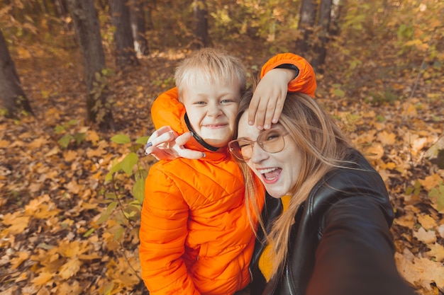 Hijo y madre están tomando selfie en cámara en el parque de otoño. Concepto monoparental, ocio y temporada de otoño.