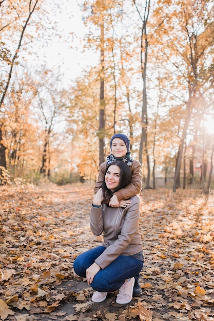 Hijo con mamá en el parque de otoño con hojas de naranja