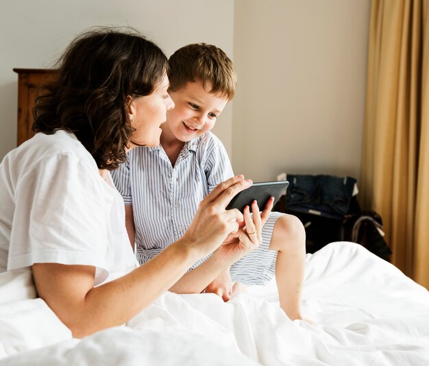 Hijo y mamá usando teléfono inteligente en pijamas