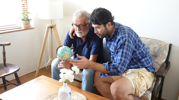 Hijo y padre senior mirando el mapa global y gesticulando juntos en la sala de estar