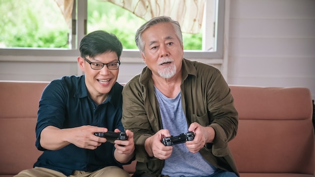 Hijo y padre viejo juegan videojuegos con controladores de joystick en la sala de estar de casa