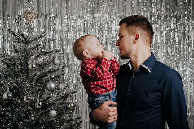 Hijo y papá, un niño pequeño en los brazos de su padre en el árbol de navidad