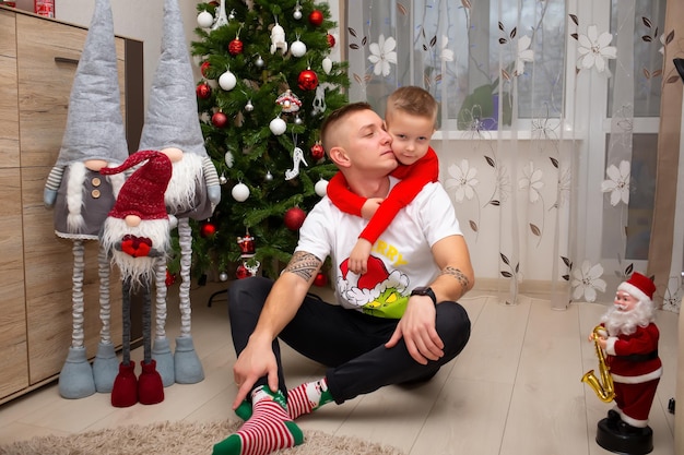 Un hijo en pijama abraza a su papá para mostrarle todos los regalos de Navidad