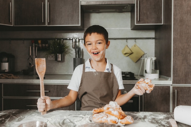 El hijo prepara un pastel, sostiene una cuchara de madera en la cocina.