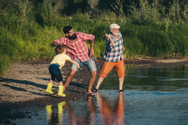 Hijo varón con padre y abuelo saltando piedras sobre el agua al hombre en diferentes edades