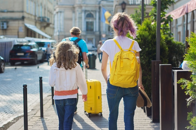 Hijos de dos niñas hijas y padre, turistas caminando por la ciudad con mochilas y una maleta. Viajes, familia, vacaciones, turismo, concepto de verano.