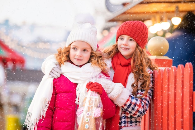 Los hijos de las hermanas pelirrojas caminan con un gran pan de jengibre en sus manos en un mercado navideño decorado festivamente en la ciudad.