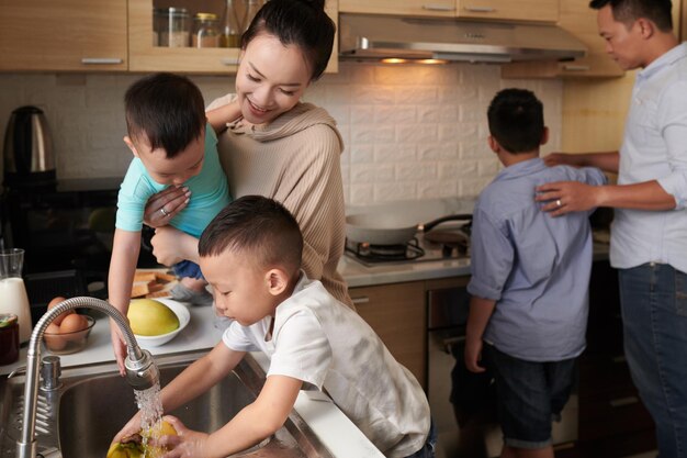 Los hijos que ayudan a la madre y al padre a preparar el desayuno están enjuagando frutas y friendo huevos