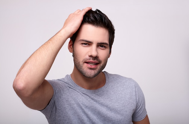 Foto hilarante chico blanco lindo toca su cabello contra una luz.