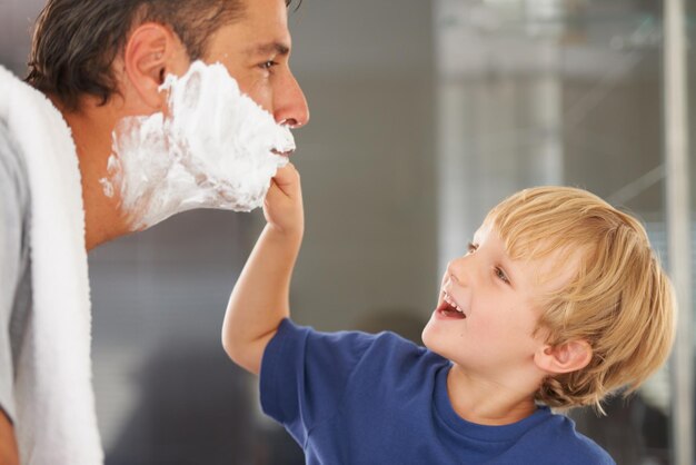 Foto hilfe beim rasieren vater und kind mit creme auf dem gesicht lächeln und bindung zu hause mit morgenroutine unterricht lernen und vater mit glücklichem sohn im badezimmer für rasieren sauber spaß oder pflege zusammen