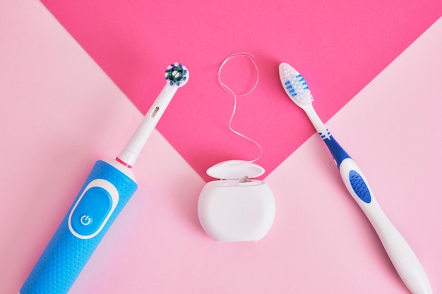 Hilo dental cepillos de dientes eléctricos y plásticos sobre un fondo rosa cuyos cepillos son más efectivos para limpiar la cavidad oral y más ecológicos