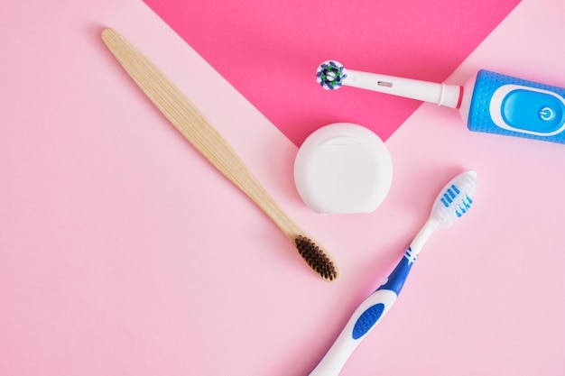 Hilo dental eléctrico de bambú y cepillos de dientes de plástico sobre fondo rosa que cepilla más eficiente o ecológico