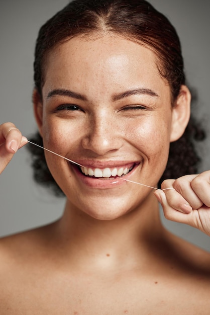 Hilo dental con hilo dental y retrato de mujer con una sonrisa en el estudio para la salud y el bienestar de la higiene bucal Cara de mujer feliz en gris para el cuidado de la salud y el aseo personal para una boca sana