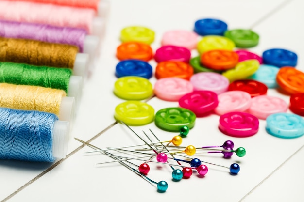 Hilos de alfileres de costura y botones de colores sobre una mesa blanca