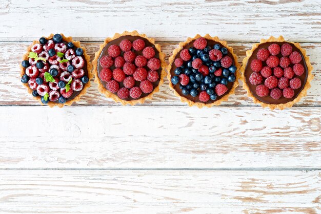 Himbeer- und blaubeertörtchen mit schokoladenganache, frischen beeren und minzblättern