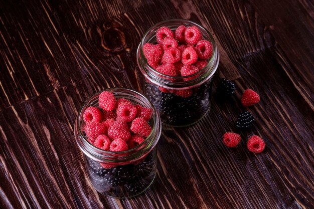 Himbeer- und Brombeersüße Bio-Saftbeeren in zwei Gläsern auf dunklem Holztisch