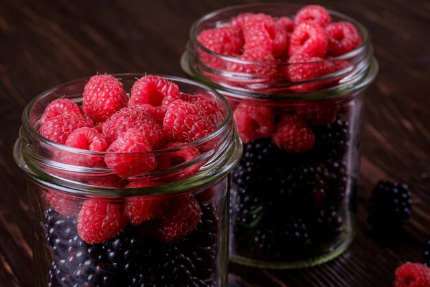 Himbeer- und Brombeersüße organische saftige Beeren in zwei Glasgefäßen auf dunklem Holztisch