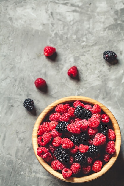 Himbeeren und Brombeeren in der Holzschale auf grauem Tisch, Weinlese