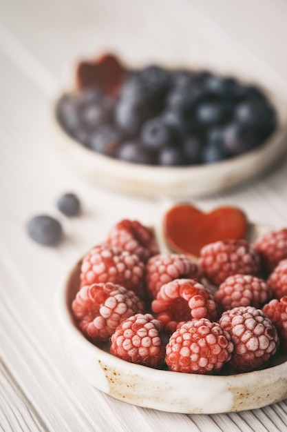 Himbeeren und Heidelbeeren in kleinen Keramikschalen mit rotem Herzdekor