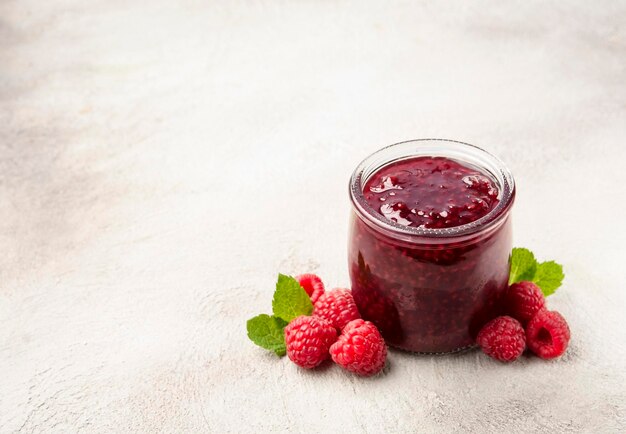 Himbeermarmelade mit Himbeerbeeren mit Minze auf Beton-Hintergrund Gesunde Lebensmittelzutat