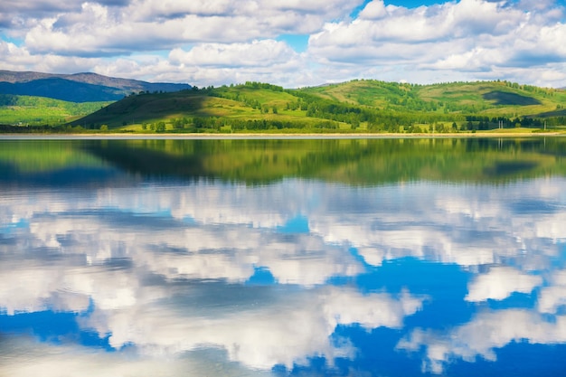 Himmel mit weißen Wolken und grünen Bergen spiegelt sich im See wider. Schöne Sommerlandschaft. Südural, Russland