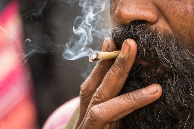 Foto hindu sadhu fumando maconha, localmente chamada de ganja, forma de cannabis sativa. usuário de tabaco. fumante permanece fumaça entorpecente de narcóticos de charutos caseiros. cigarro fechar. aperto do opiáceo.