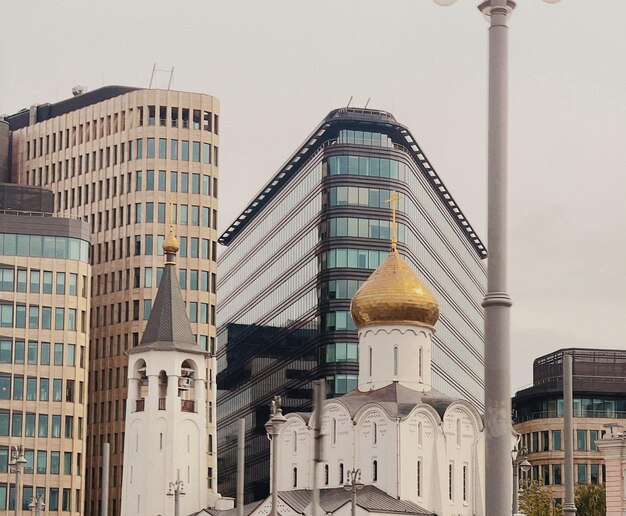 Hinter einer Kirche mit einer goldenen Kuppel steht ein Gebäude mit Glasfassade.