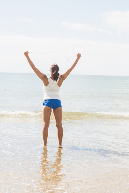 Hintere Ansicht der dünnen jungen Frau, die auf dem Strand im hellen Sonnenschein steht