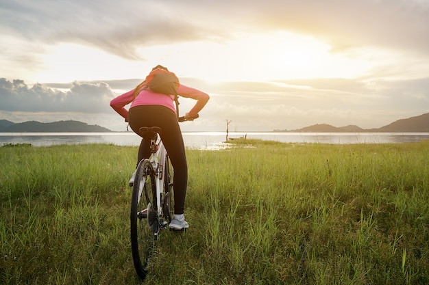 Hintere Ansicht der RadfahrerreitMountainbike, die mit Fahrrad an auf Grasspur bei Sunris aufwirft