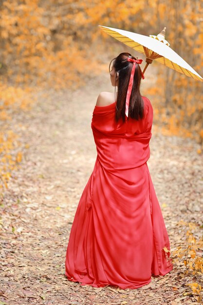 hintere Ansicht der schönen asiatischen Frau im chinesischen Kostüm des roten Kriegers mit altem Regenschirm