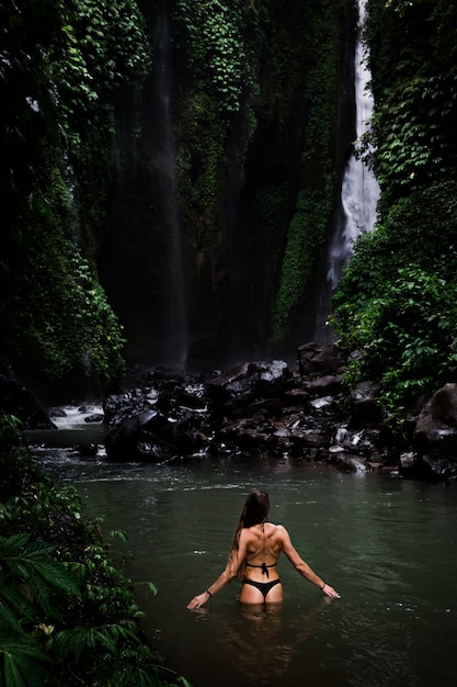 Hintere Ansicht der Schönheit badend und im natürlichen Swimmingpool vor Wasserfall im Naturpark auf Tropeninsel entspannend. schöner Wasserfall im Bali, Indinesien
