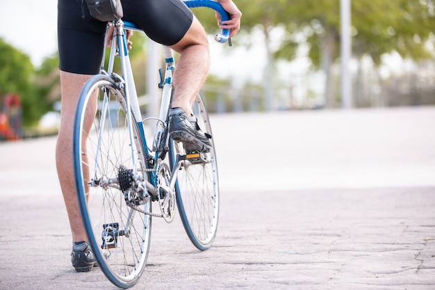 Hintere Ansicht des jungen kühlen männlichen Radfahrers in der Sportkleidung, die das Radfahren in schönen Stadtpark vorbereitet