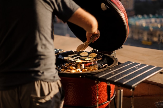 Hintere Ansicht des Mannes Frischgemüse auf dem Grillgrill am sonnigen Tag kochend