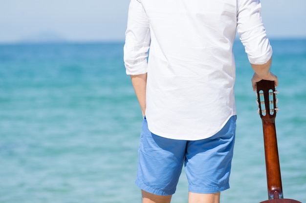 Hintere Ansicht des Mannes mit Gitarre am Strand.