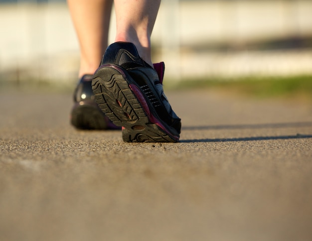 Hintere Ansicht einer Frau, die in Turnhallenschuhe auf einem Weg geht