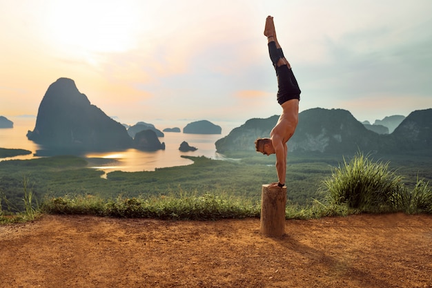 Hintere Ansicht einer Yogahaltung. Glücklicher Mann in der schwarzen Kleidung, welche die Yogahaltung steht auf seinen Händen auf dem Baum tut.