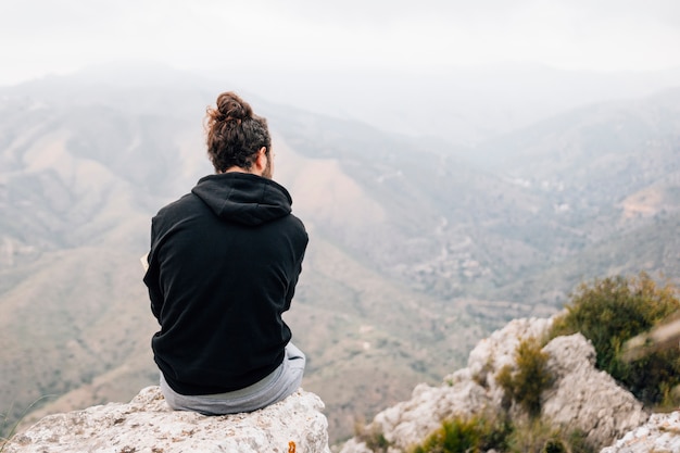 Hintere Ansicht eines männlichen Wanderers, der auf den Felsen übersieht Bergblick sitzt