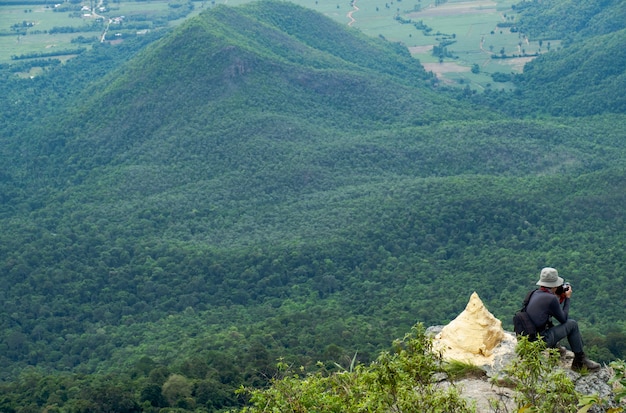 Foto hintere ansicht von den männern, die auf klippe sitzen und machen ein foto gegen berg und baum